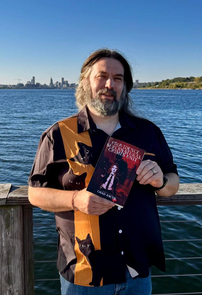 The author posed with the book 'Providence Supernatural Crimes Unit' with the Providence skyline behind him. 